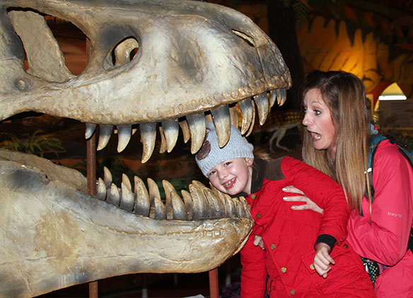 Picture of school teacher amusingly holding pupils head in dinosaur skeleton mouth